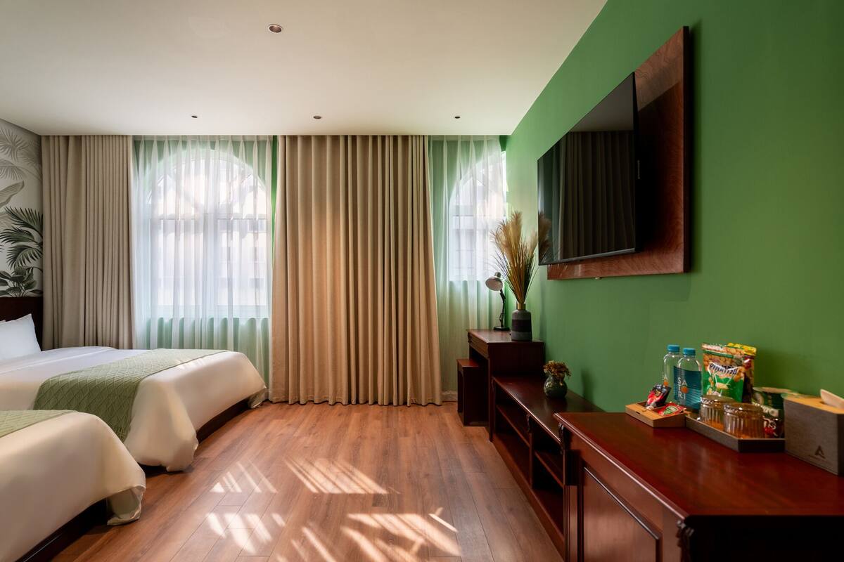 Une chambre d’hôtel avec deux lits, un bureau, un miroir et une télévision.