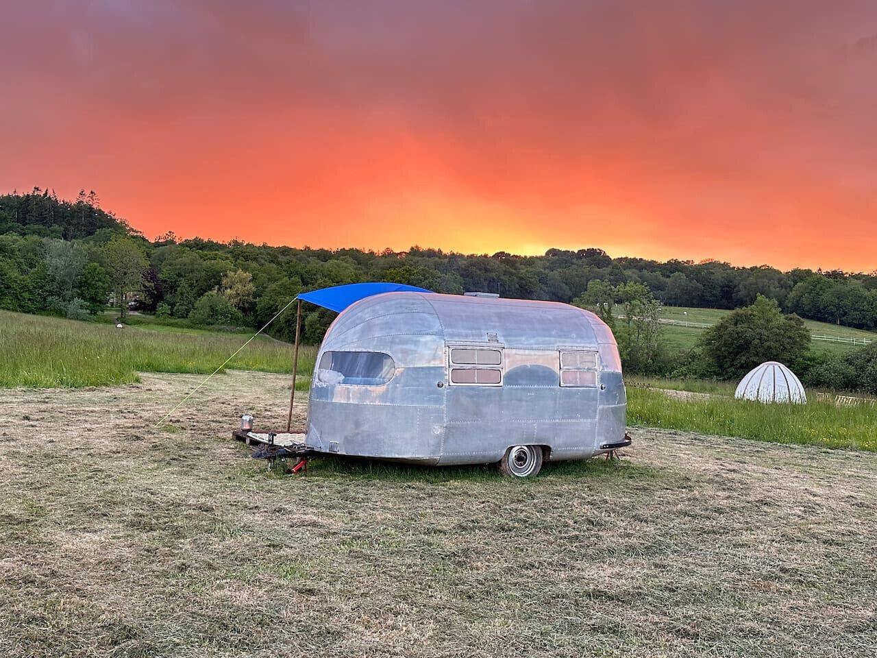 A vintage trailer with a blue awning parked on a grassy field.