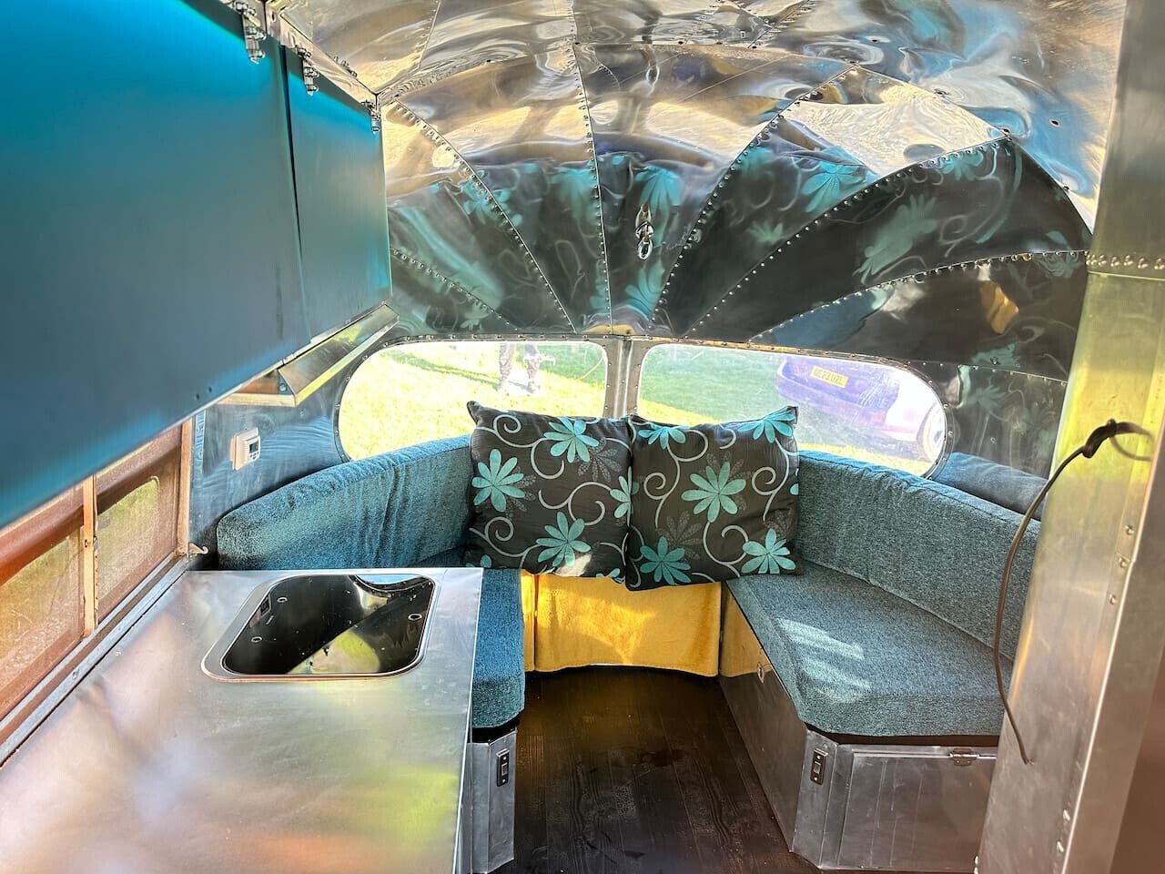 Interior compacto e bem iluminado, com banco, mesa pequena e janela com vista para o exterior.