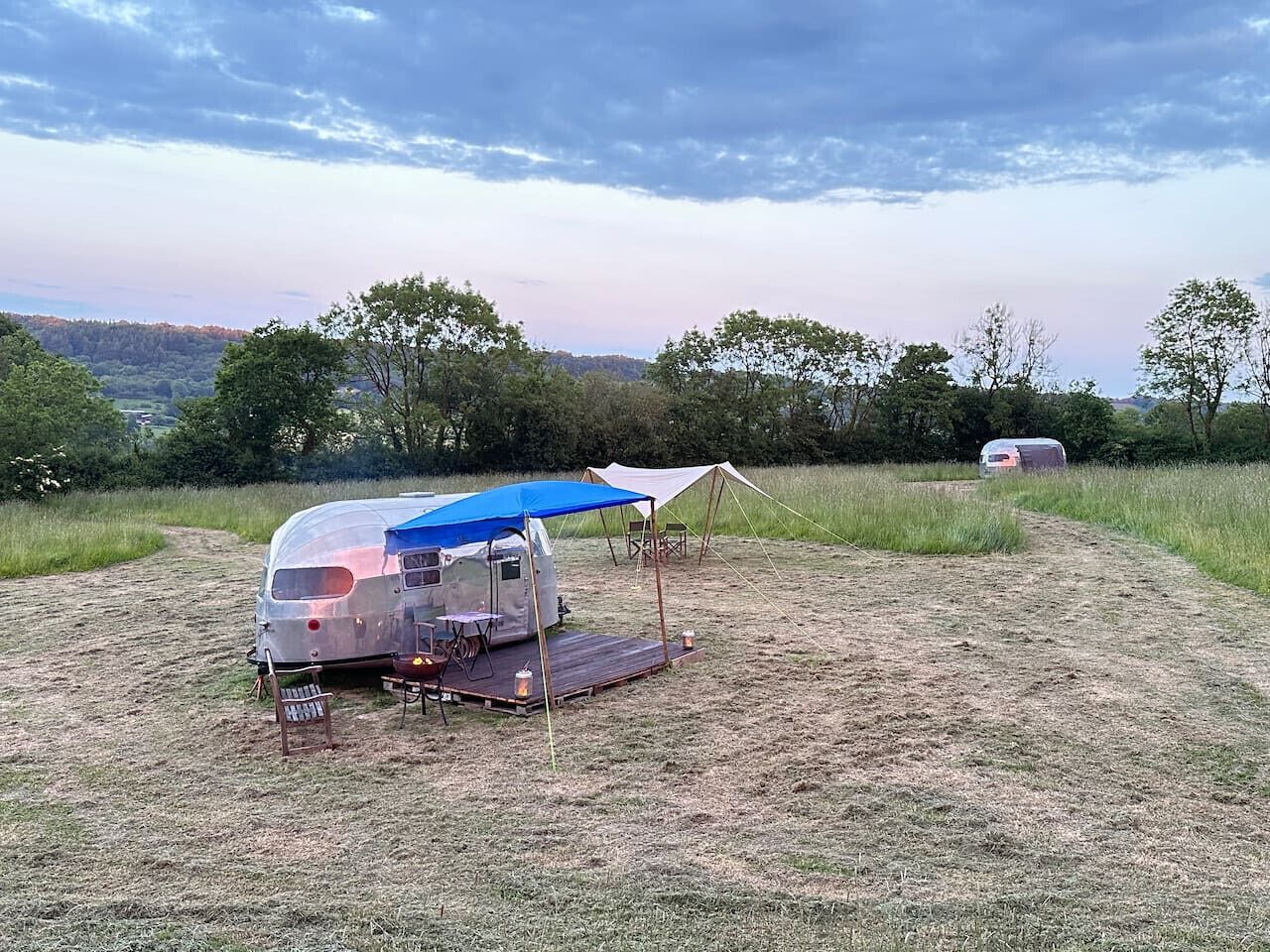 Un vehículo recreativo (RV) con un toldo azul y una pequeña mesa montada en un campo cubierto de césped.