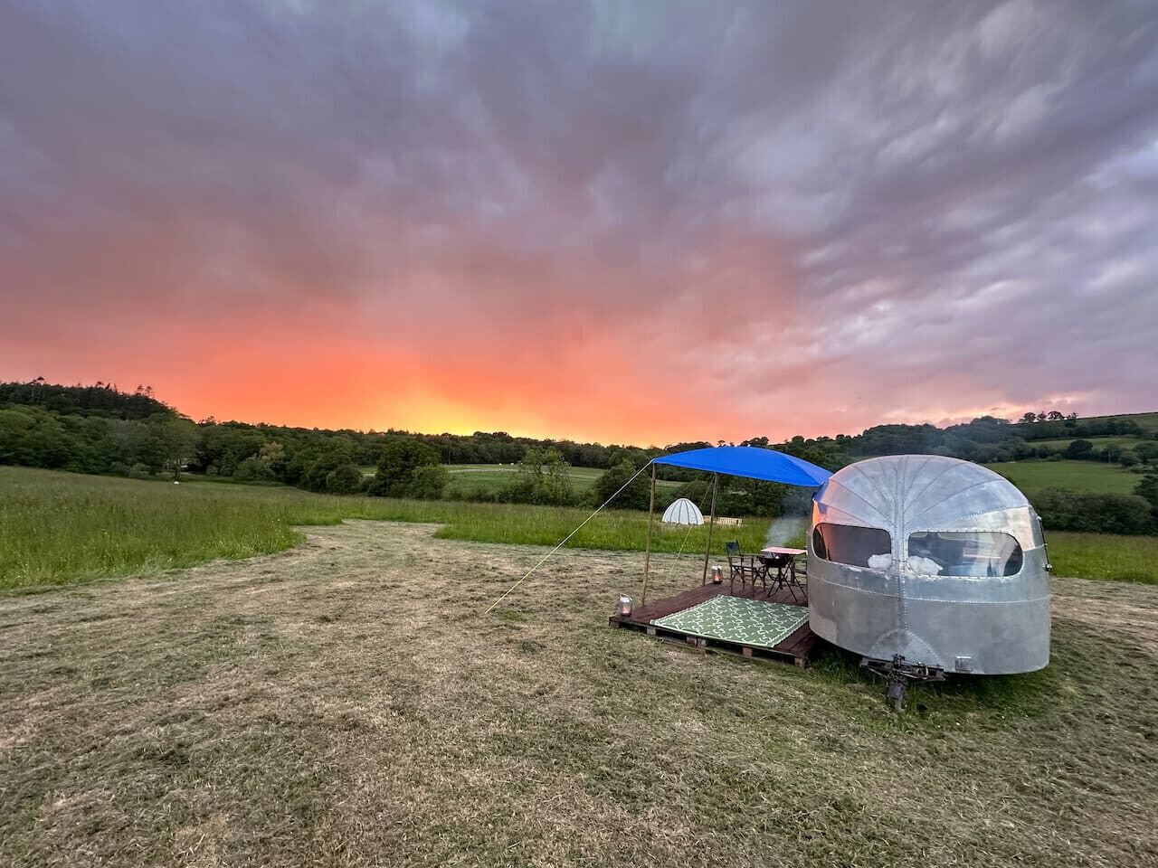 Un campeggio con un camper e una tenda sotto una volta celeste, sullo sfondo un tramonto.