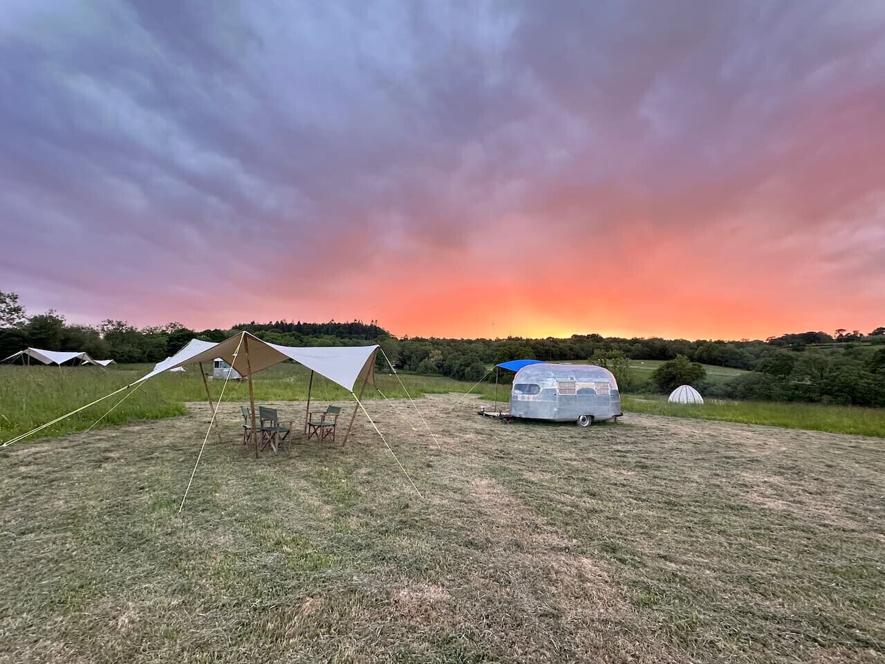 Un camping con tiendas de campaña y una caravana instalado en un campo de césped.