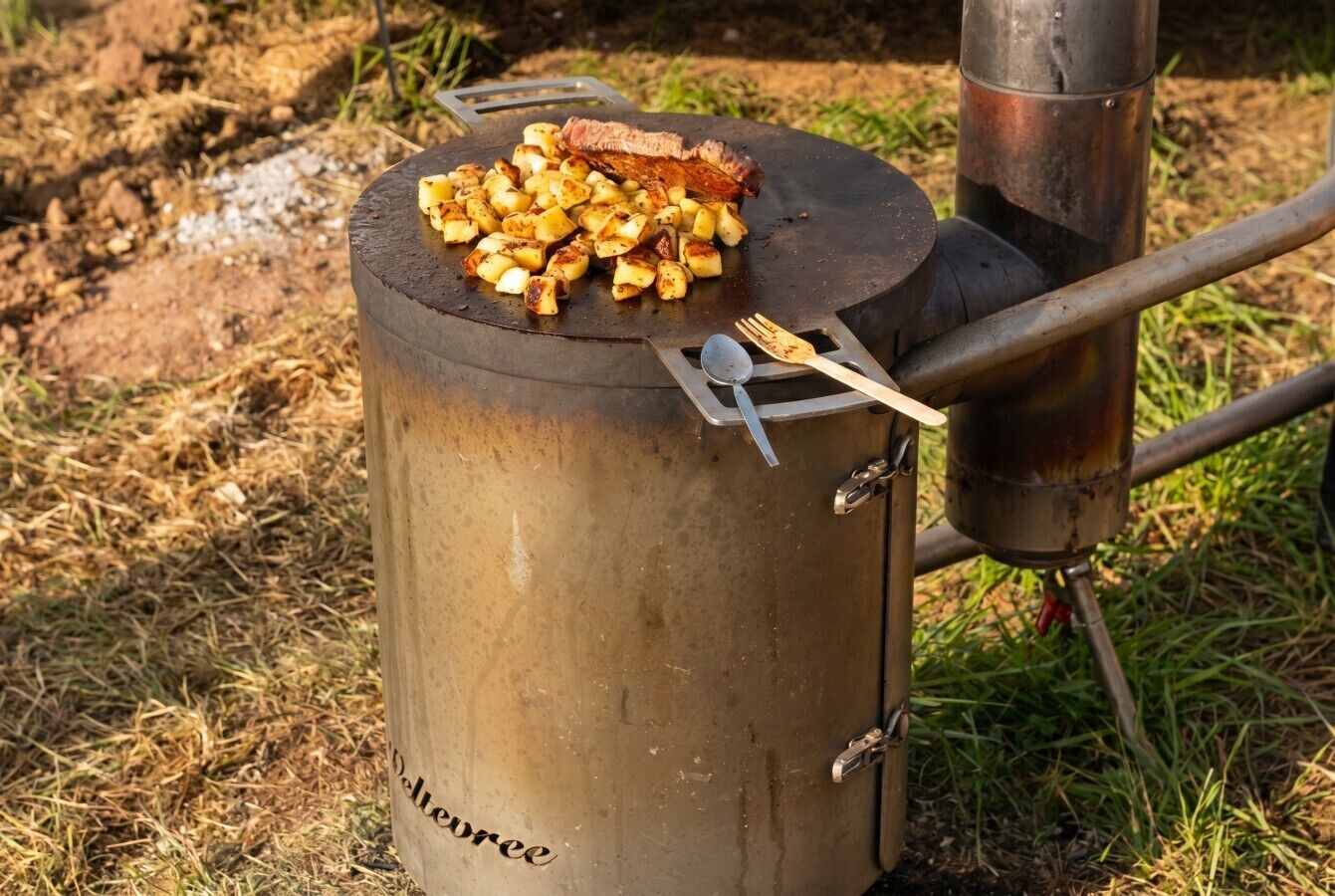 Et transportabelt kogebord med en steak og kartofler ovenpå, omgivet af græs.