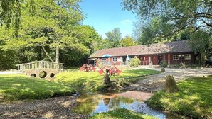 A rustic building with a brick facade, a small stream, and a wooden bridge.