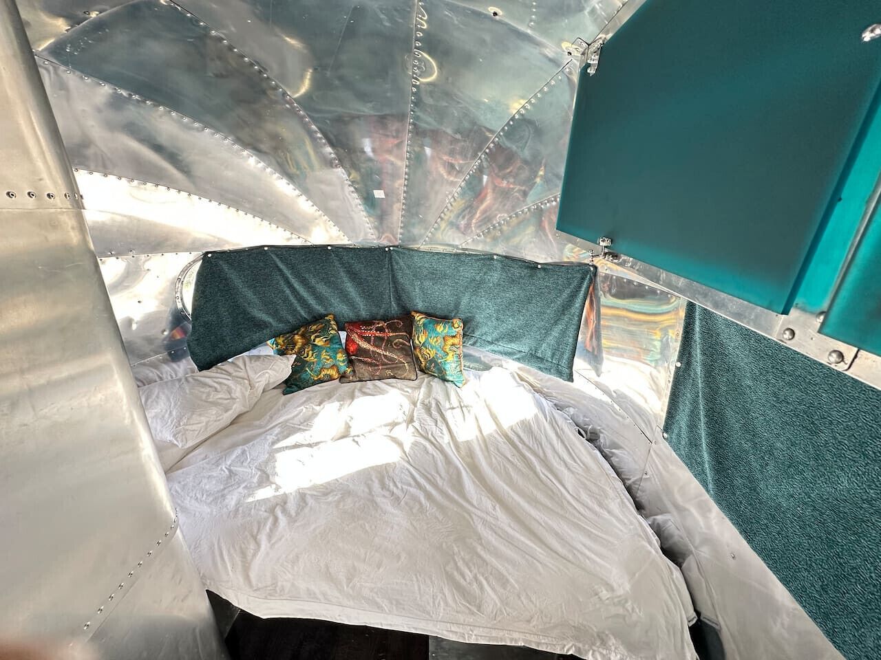 A bed with a white sheet and colorful pillows in a metallic room with teal accents.