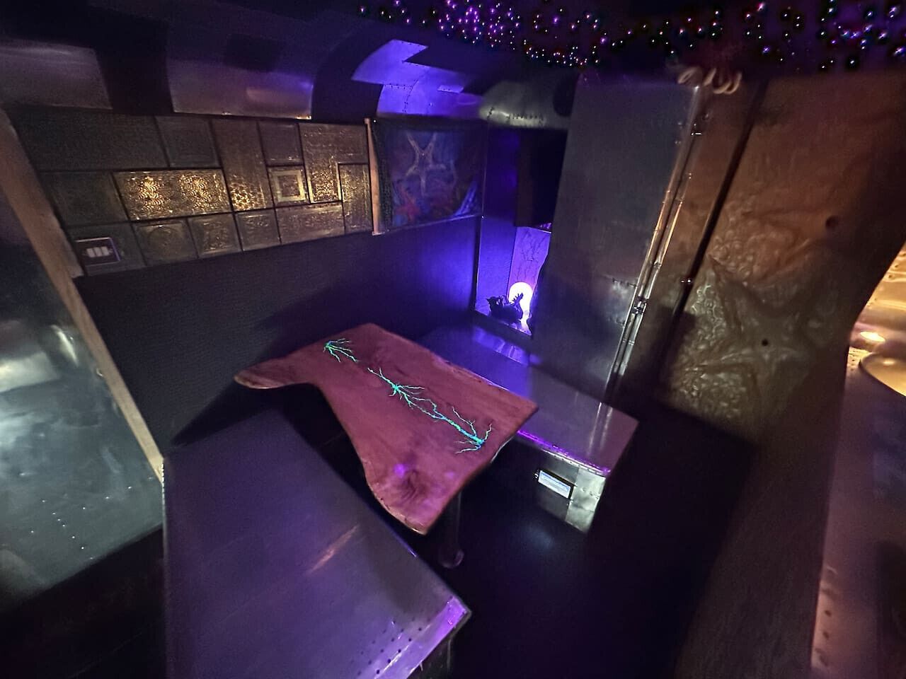 Une pièce faiblement éclairée, avec une table, un banc et un mur orné d’un motif texturé.