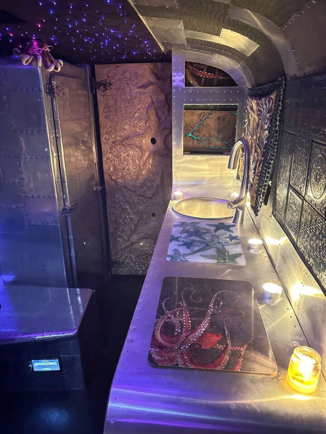 Ein Badezimmer mit Marmorwand, Waschbecken und Spiegel. Ein kleines Regal zeigt eine Kerze und ein dekoratives Objekt.