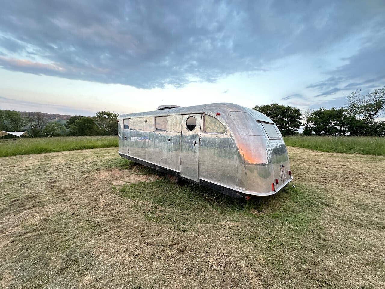 A vintage trailer with a rounded front and multiple windows, parked on a grassy field.