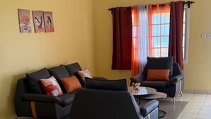 Ein Wohnzimmer mit einer Couch, einem Couchtisch und zwei Sesseln. An der Wand hängen drei gerahmte Bilder.