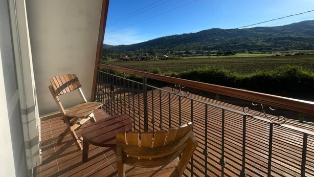 Un balcón con mobiliario de madera, vista a un viñedo y una montaña al fondo.