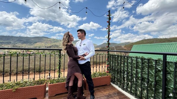 Una pareja de pie en un balcón con vista a un paisaje verde y colinas.