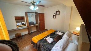 Un dormitorio con cama, armario, ventilador de techo, taburete pequeño y mesita de noche con lámpara.