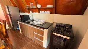 Cocina compacta con encimera negra, refrigerador de acero inoxidable y estufa a gas.