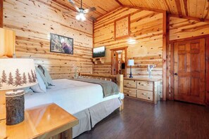 A wooden cabin interior with a bed, dresser, and a television on the wall. - 6-Bedroom Mountain Cabin with Heated Indoor Pool & Game Room, Sleeps 14 (Sevierville)