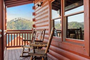 Una terraza de madera con una mecedora y una mesa, con vistas a un paisaje boscoso.