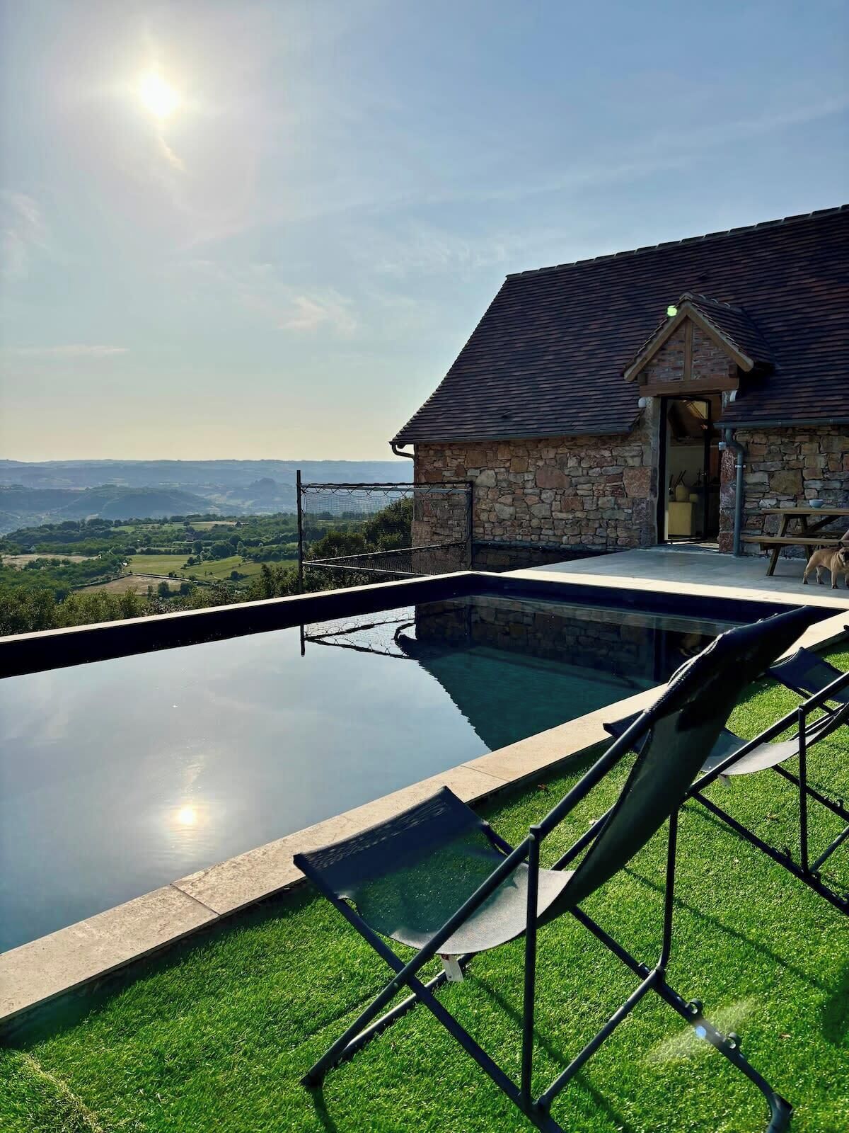 Une piscine avec un toboggan, un bâtiment en pierre et une vue sur la campagne.
