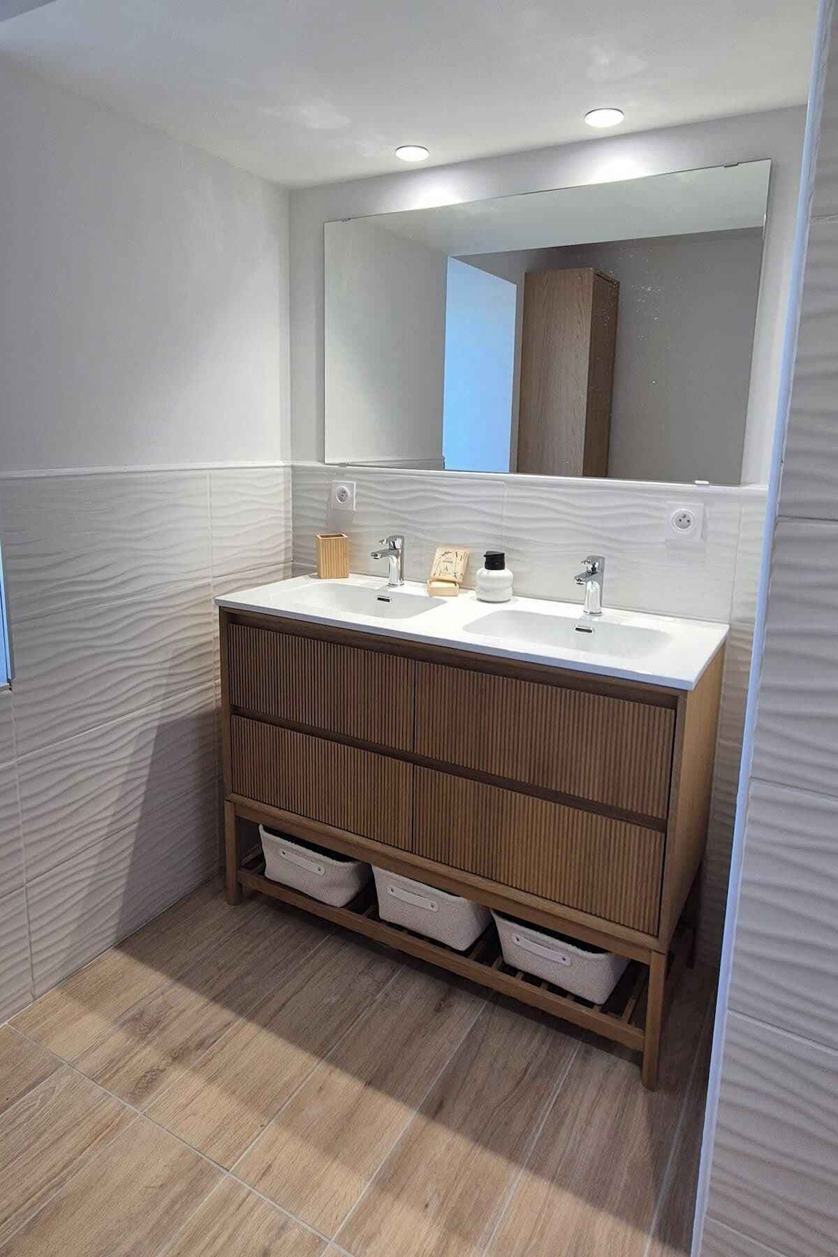 A modern bathroom with two sinks, a large mirror, and built-in storage drawers.