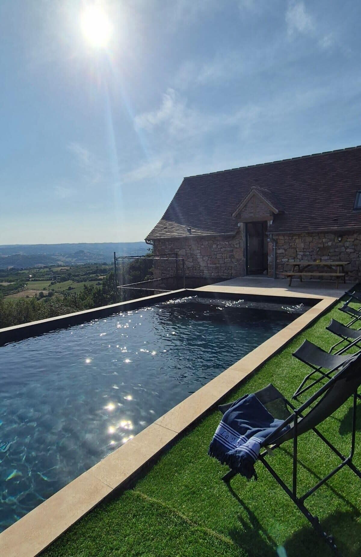 A swimming pool with a stone building in the background, a clear sky, and a view of the countryside.