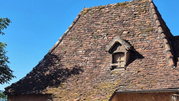 Une maison de campagne en pierre, dotée d’un toit à forte pente, d’une petite lucarne et d’une porte en bois.