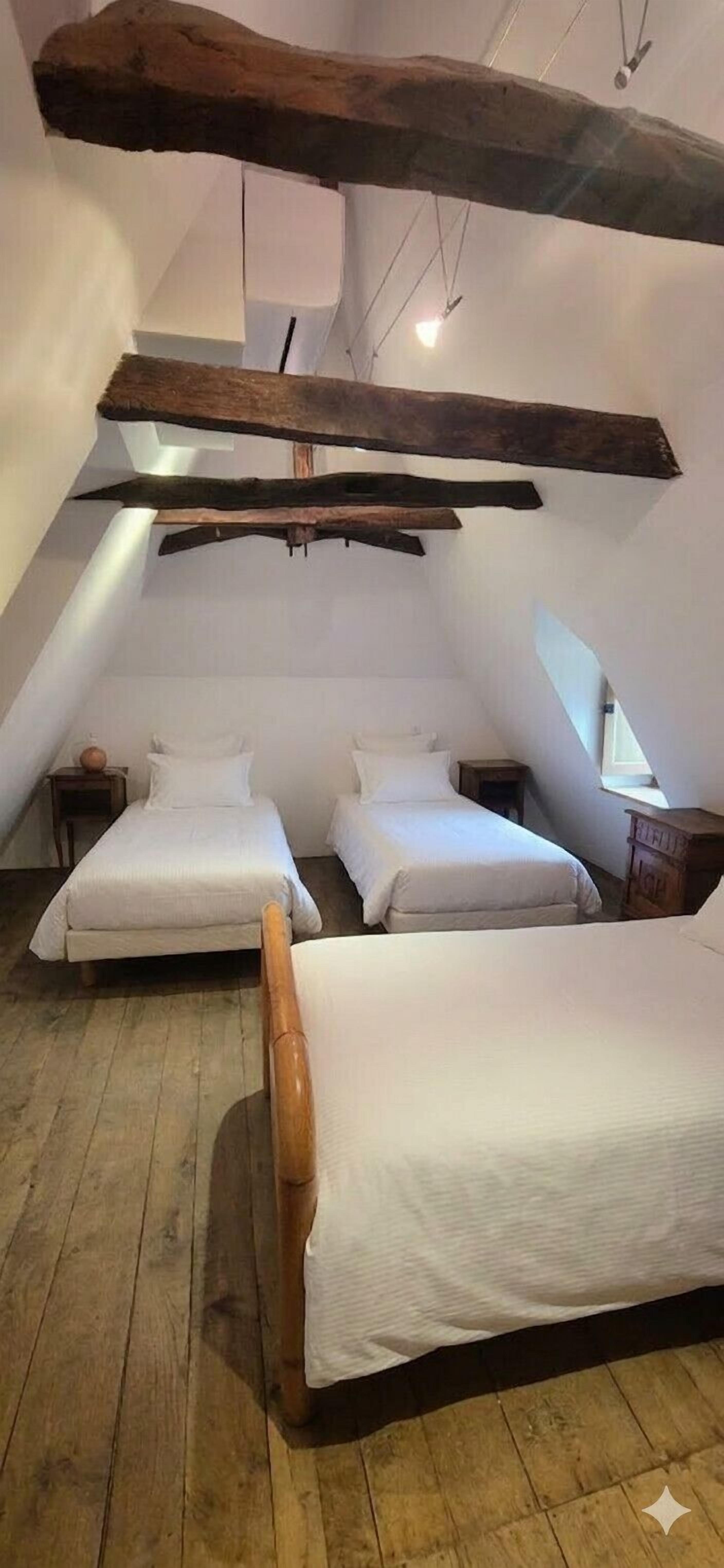A small, cozy attic bedroom with two beds, wooden beams, and a sloped ceiling.