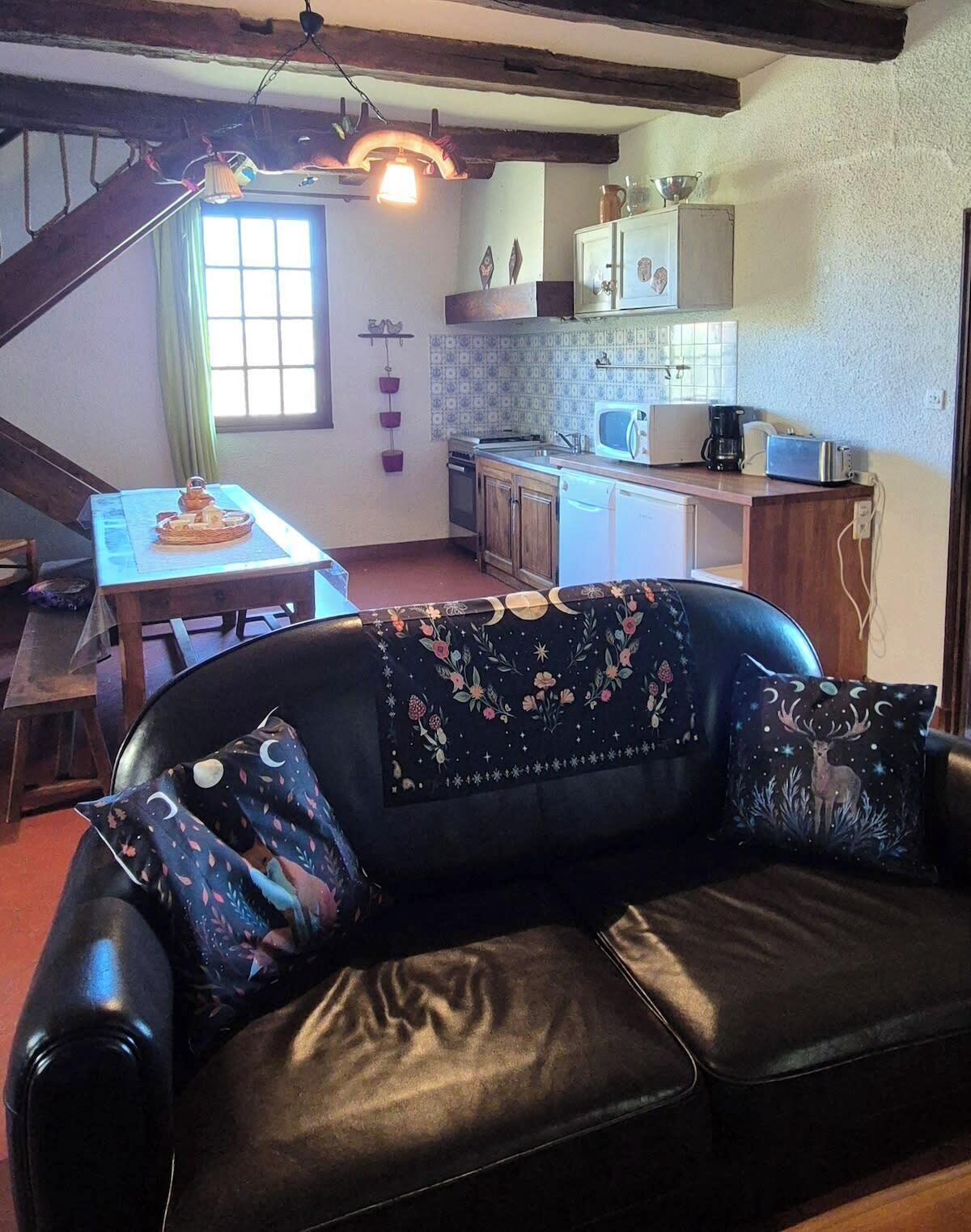 Een gezellige woonkamer met een zwarte leren bank, een eettafel en een keuken met basisapparatuur.