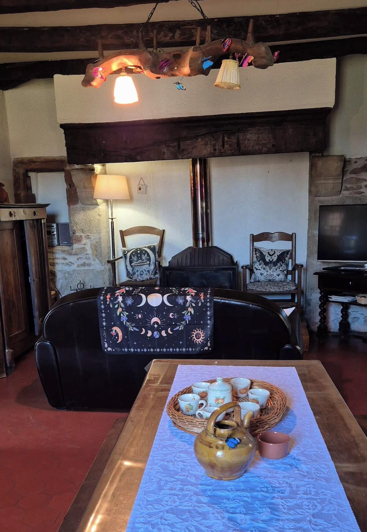 Ein gemütliches Wohnzimmer mit Kamin, einer schwarzen Ledersofa, einem Couchtisch aus Holz mit Teeservice und einem Fernseher auf einem Holzboden.