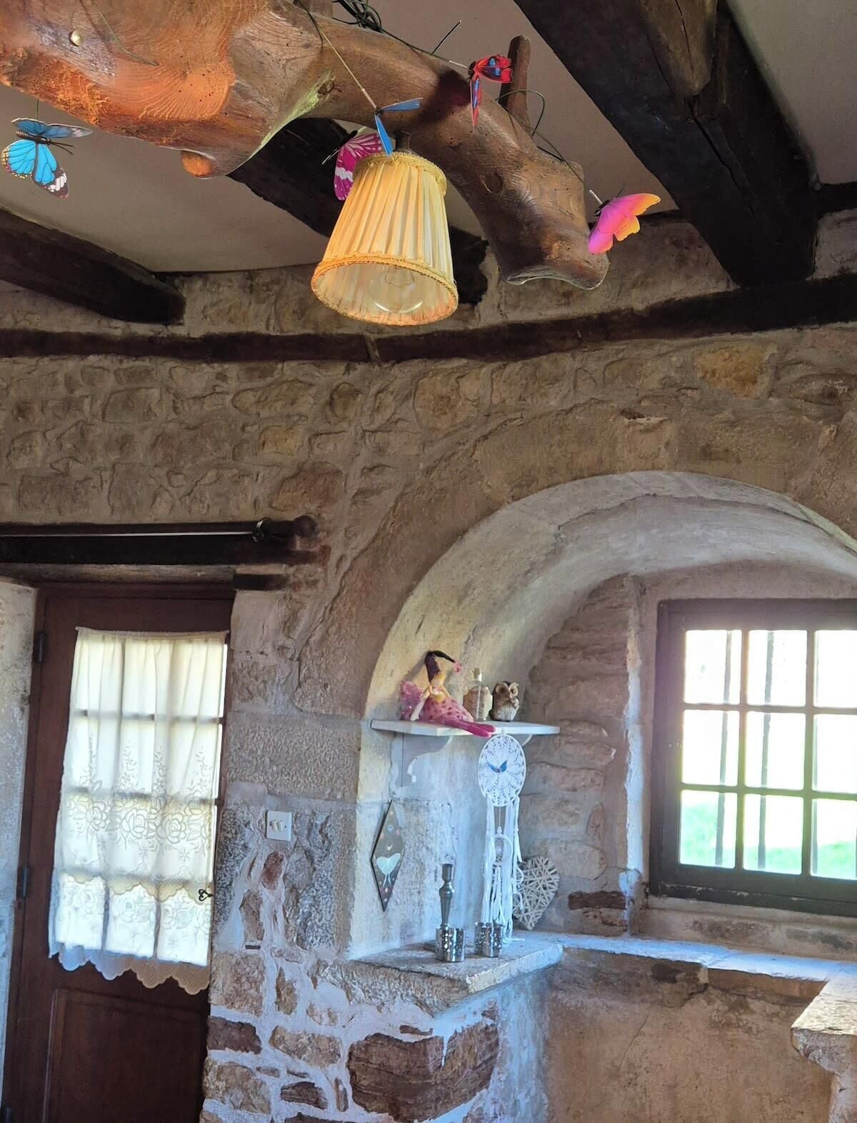 Interior rústico de piedra con techo de madera, ventana con vistas y estante con adornos.