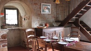 Un coin repas rustique avec un mur en pierre, une table en bois, des chaises et un escalier.