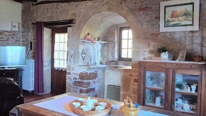 Une pièce rustique avec un mur en pierre, une table en bois sur laquelle est disposé un service à thé, une armoire aux portes vitrées et un tableau encadré accroché au mur.