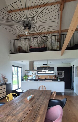 Une cuisine moderne dotée d’un îlot central, d’un coin repas avec une table en bois et d’un escalier menant à un niveau supérieur.