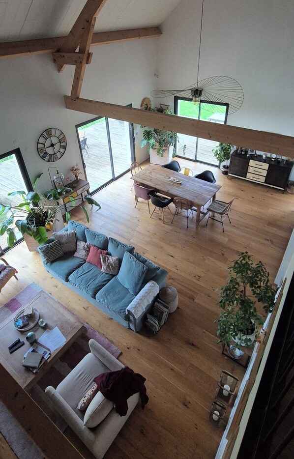 Un vaste espace de vie doté d’un plancher en bois, d’un canapé bleu, d’une table à manger avec des chaises et de grandes fenêtres.