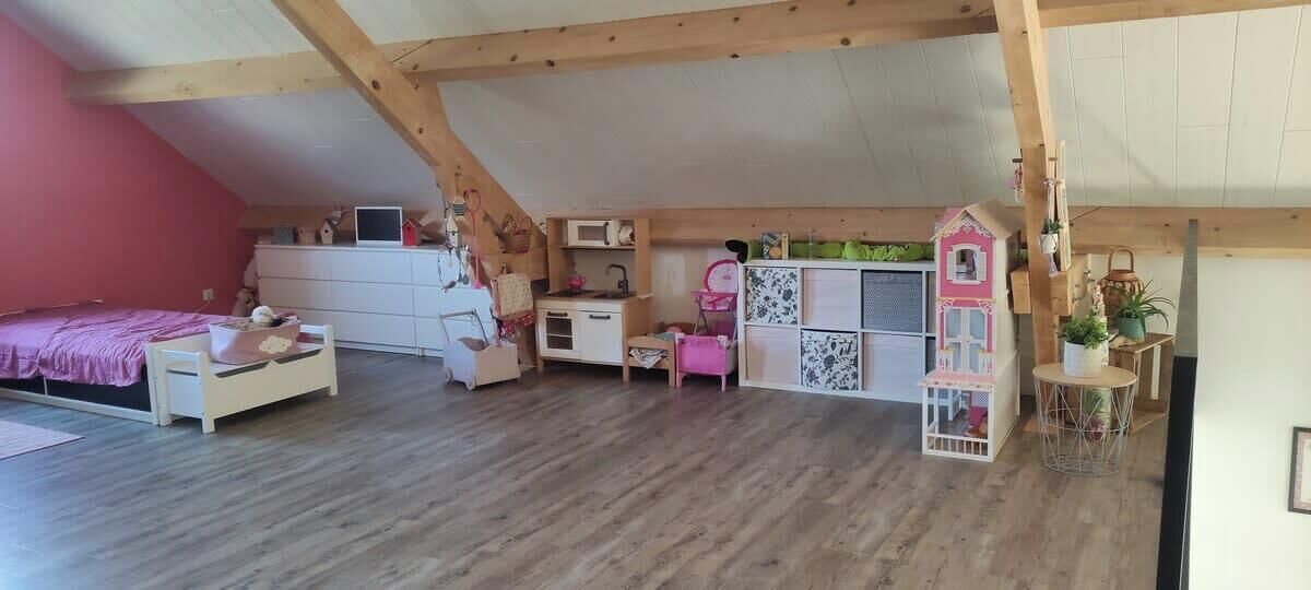 Een gezellig zolderkamer met een schuine plafond, een bed, een bureau en een poppenhuis.