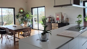 Une cuisine moderne dotée d’un îlot central, de grandes fenêtres et de plantes en pot.