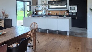 Une cuisine moderne avec des meubles blancs, une table à manger en bois et un balcon doté d’une rambarde noire.