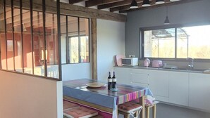 A modern kitchen with a dining area, wooden beams, and a view of the outdoors. - La Bergerie de la Borie, piscine, près Rocamadour (Miers)