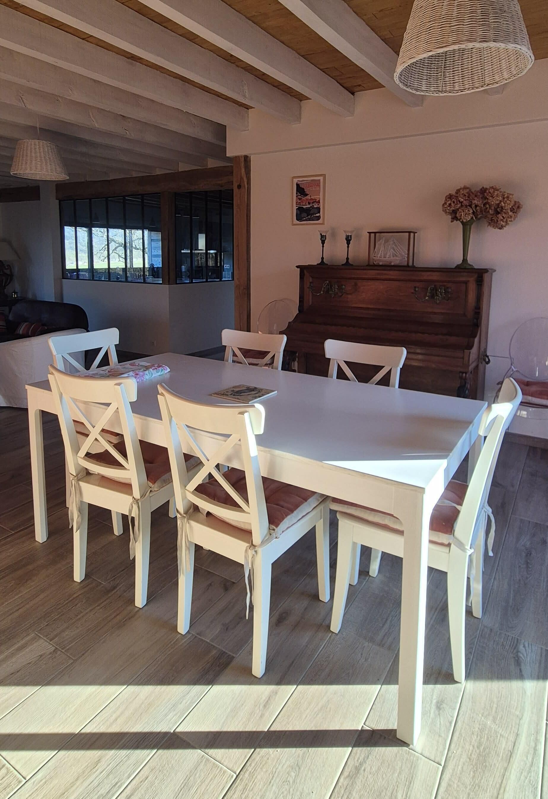 A dining area with a white table and chairs, a wooden piano, and a hanging light fixture.