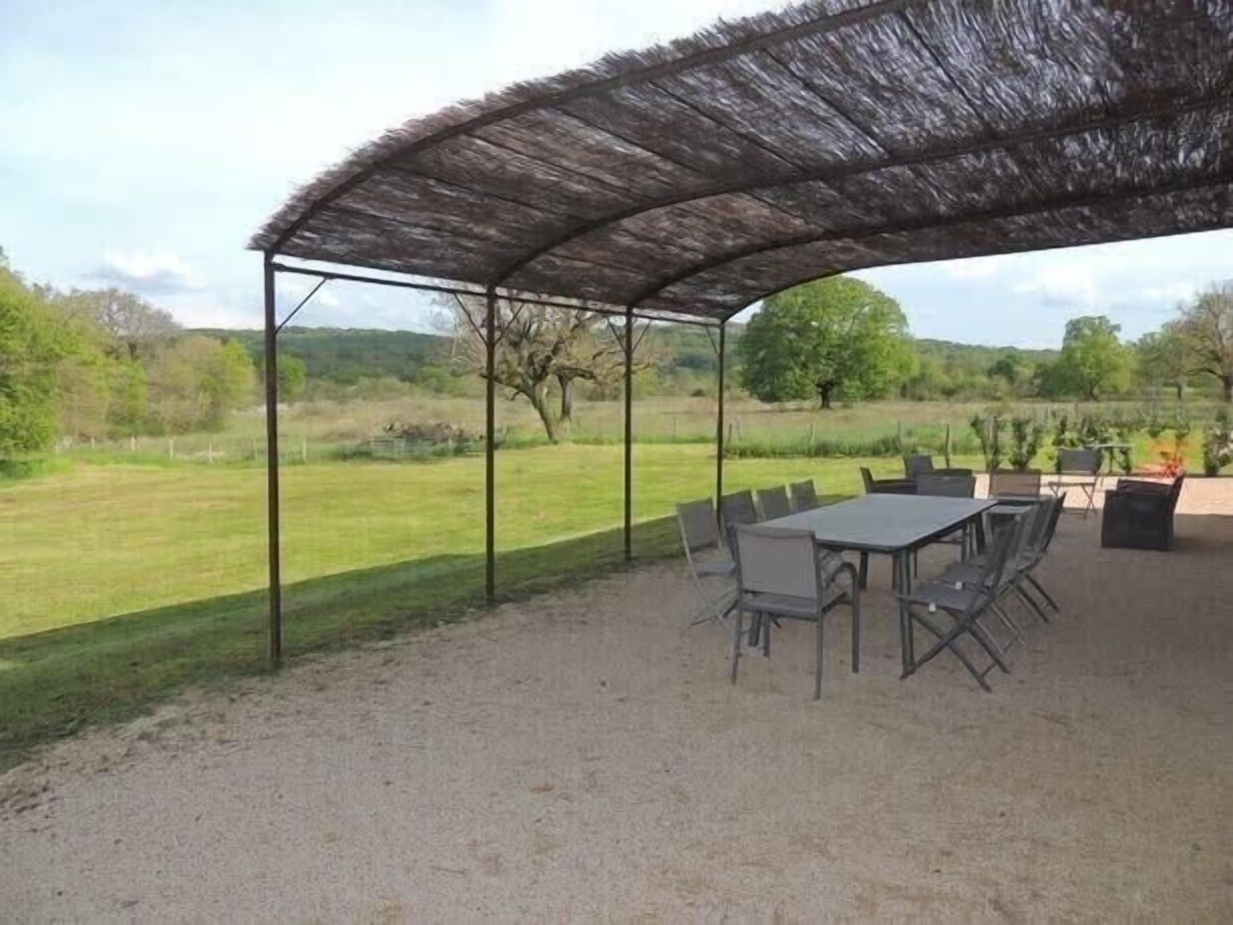 Un patio al aire libre con una mesa y sillas, rodeado por una estructura de techo de paja.