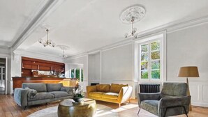 A spacious living room with a wooden floor, a round coffee table, a sofa, and a chair. There is a kitchen in the background with wooden cabinets and a window. - Maison de la source, swimming pool, 10 min padirac (Alvignac)