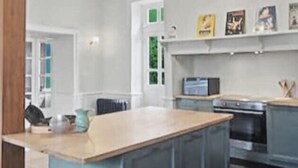 A kitchen with a large island, wooden stools, and a hanging light fixture. - Maison de la source, swimming pool, 10 min padirac (Alvignac)
