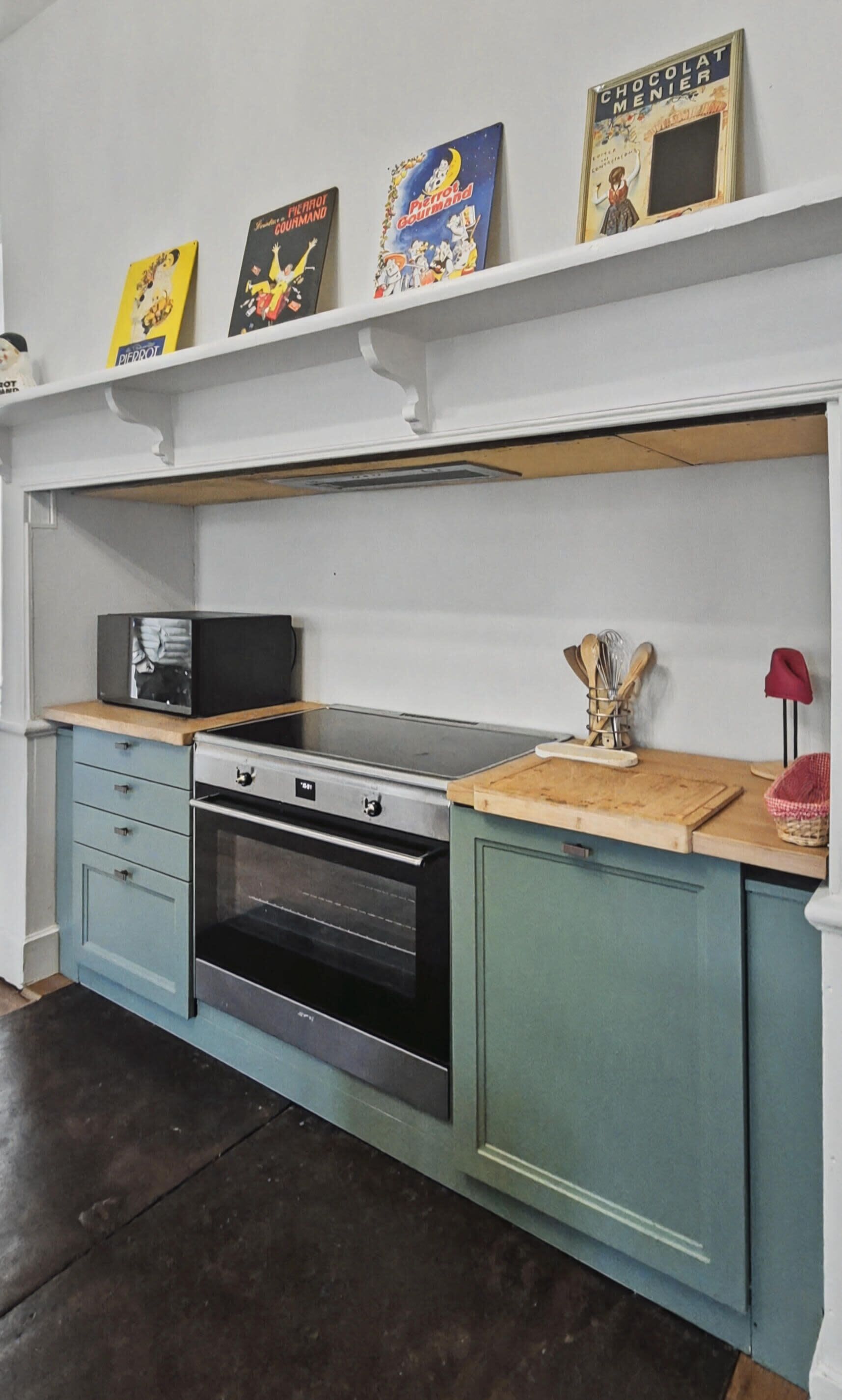 A kitchen with a built-in oven, a microwave, and a wooden countertop. There are three books on the shelf above the countertop.