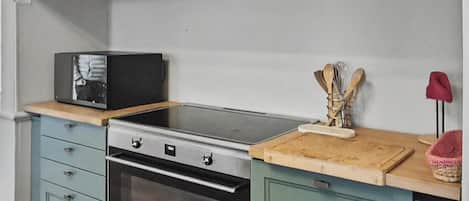 A kitchen with a built-in oven, a microwave, and a wooden countertop. There are three books on the shelf above the countertop.