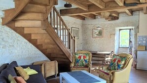 A rustic interior with a wooden staircase, a sofa, a coffee table, and two chairs with colorful cushions. - The Parrot House (Floirac)