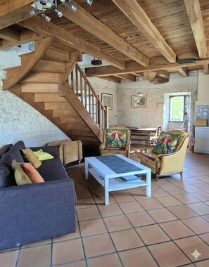 A rustic interior with a wooden staircase, a sofa, a coffee table, and two chairs with colorful cushions. - The Parrot House (Floirac)