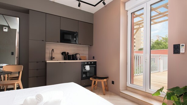 A compact kitchen with modern appliances, a dining area with a wooden chair, and a large sliding glass door leading to an outdoor balcony.