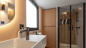 A modern bathroom with a large white sink, a mirror, and a glass-enclosed shower area.