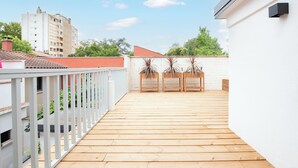 A rooftop terrace with wooden flooring, white railings, and potted plants.