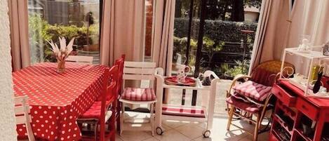 Un patio couvert avec une table et des chaises, une petite table avec une carafe et un verre, et un meuble de rangement rouge.