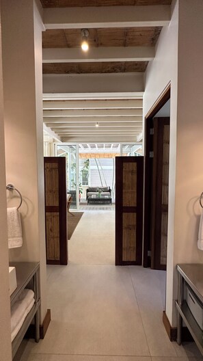 Un pasillo con techo de madera, vistas a una sala de estar con sofá y mesa de centro, y un baño con perchero.