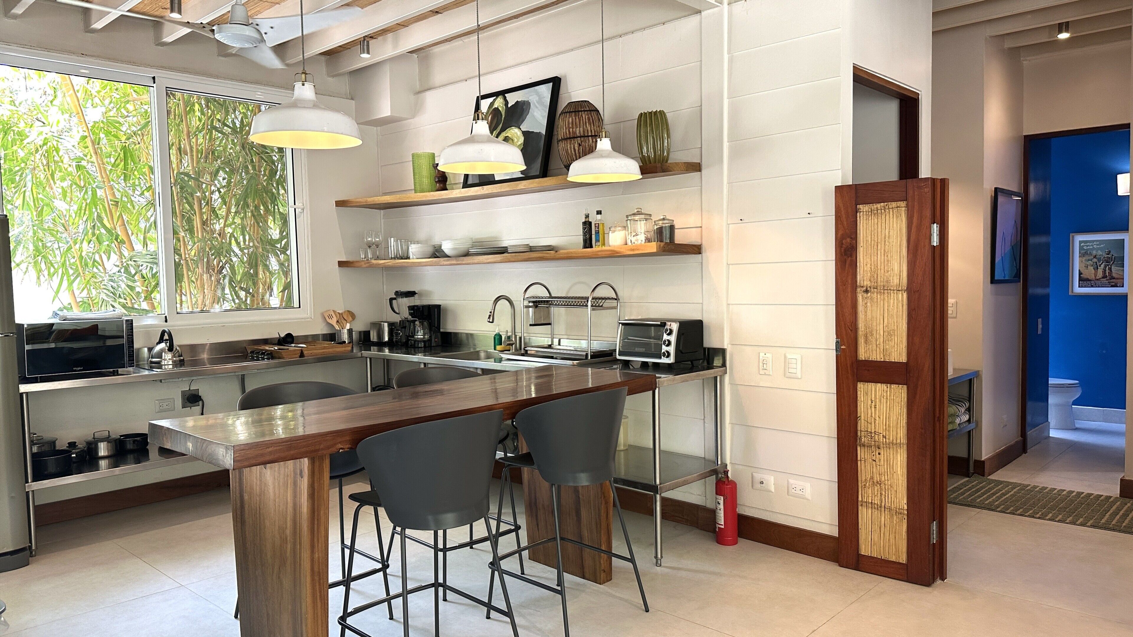 A modern kitchen with a bar area, stainless steel appliances, and a view of greenery outside.
