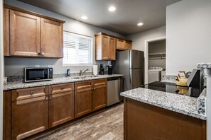 A modern kitchen with wooden cabinets, granite countertops, a stainless steel refrigerator, a microwave, and a stove.